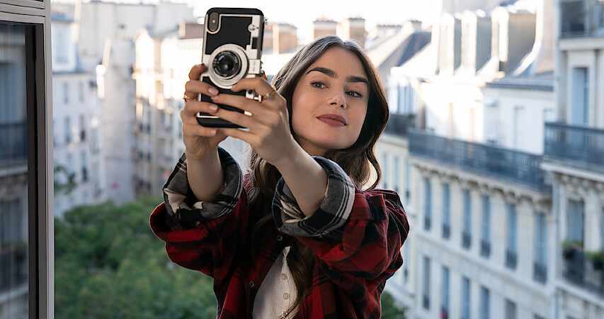 Lily Collins as Emily Cooper taking a selfie on her balcony in Paris